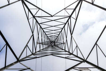 High voltage pylon against cloudy sky. Bottom view. Pattern of metal architecture.の写真素材