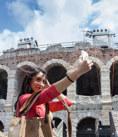 Young woman tourist, with her fashion cork bag, taking selfie photo in Verona (Italy). In background the famous Arena.の写真素材