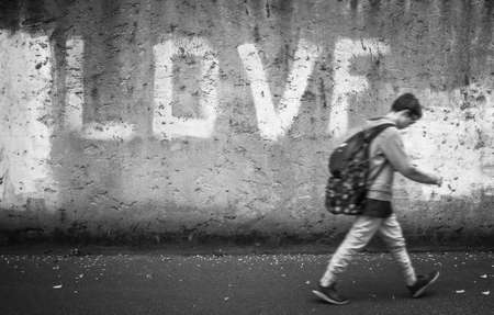 Schoolboy walking down the street with head bowed; love on background. Back to school.の写真素材