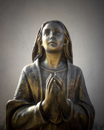 Holy Mary statue bronze that prays with folded hands, in the background a gray wall. It can be used for events, concepts and backgrounds.のeditorial素材