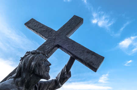Bronze statue of Jesus carrying his cross, on the way to his crucifixion. Ideal for the easter concept, resurrection and other. Blue sky with white clouds on background.の写真素材