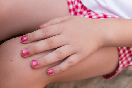 Close - up of Hand of a baby girl with pink nail polish, in a summer day.の写真素材