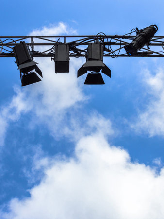 Spotlights for outdoor stage on the metal construction against a blue sky and clouds. Space for text.の写真素材
