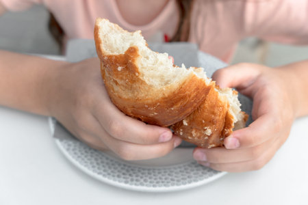Pretty little girl eats a fresh croissant for breakfast. Portrait of cute girl with yummy face enjoy...