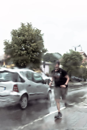 Man running during rainy day in a sidewalk. Defocused.