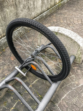 A damaged bike wheel is all that is left of a bicycle chained to a bike stand. Stolen bicycle. Chained bicycle wheel.の写真素材