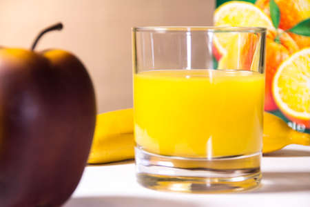 A glass half full of orange juice, an apple and a banana.の写真素材