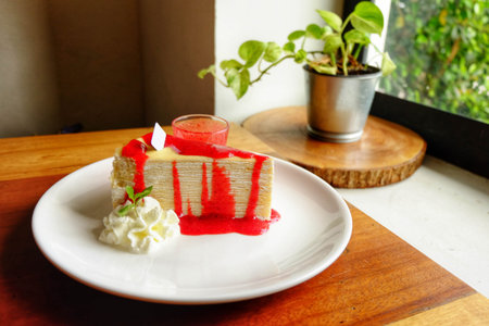 Crepe cake with cream and strawberry on top and sauce in ceramic cup on white plate.の写真素材