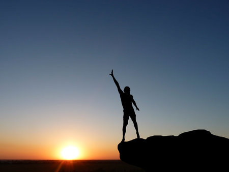silhouette of a man at the top of the mountain against the skyの写真素材