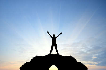 woman on a mountain top his arms in hand against the sunny skyの写真素材