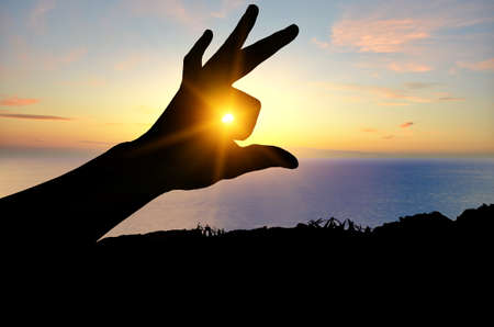 silhouette of a human hand on the background of the sea beach, through the fingers of which the sun shines brightlyの写真素材