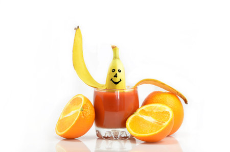 Banana is in a glass of tomato juice surrounded by orangesの写真素材