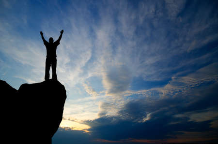 silhouette of a businessman with a laptop in hand is on top of a mountain in the sky with clouds.の写真素材