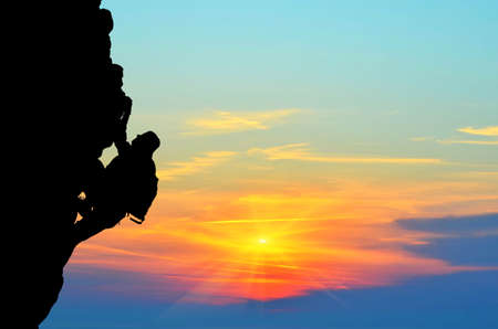 silhouette of a person without insurance climbs the rock in the background of the sunsetの写真素材