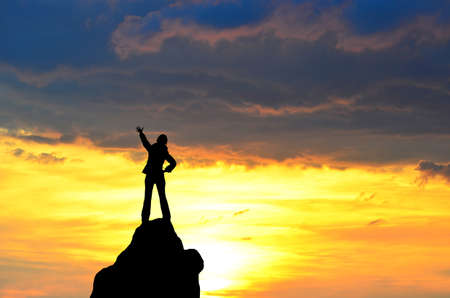silhouette of a girl standing on a cliff side in his arms against the sunsetの写真素材
