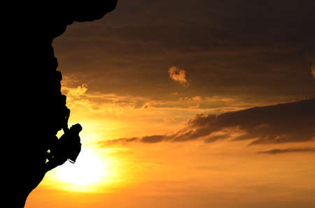 silhouette of a person without insurance climbs the rock in the background of the sunsetの写真素材