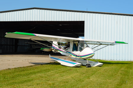 Single engine float plane parked on grass in front of a hangar with a clear blue sky.