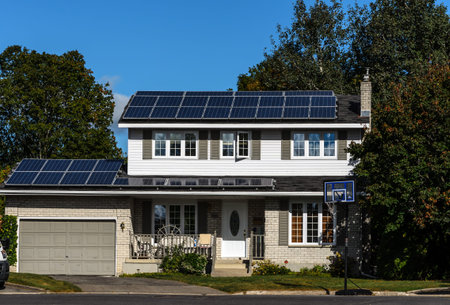 Solar panels on a suburban house rooftop with trees and blue sky background