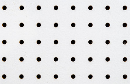 Close-up of symetrical rows and columns of holes on a white pegboard