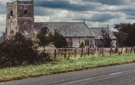 Old English church alongside a country road under a stormy skyの写真素材