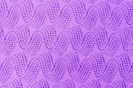 Close-up above view of waves of blue cascading dots on light purple fabric layed out flat on a white...