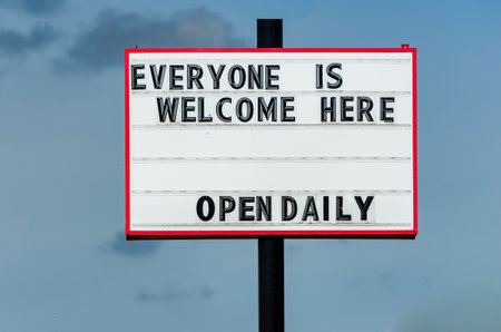 Retail open sign welcoming everyone during the pandemic restrictions, taken during the day against a light blue sky.の写真素材