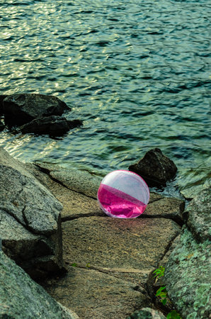 Purple and white beach ball trapped on rocks  by waves at the edge of the waterの写真素材
