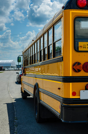 Rear left view of a school bus behind a car under a cludy blue skyの写真素材