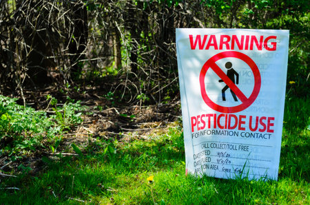 Sunlit Pesticide Warning sign next to forest edgeの写真素材