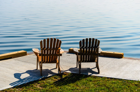 Two Adirondack chairs facing the water's edge on a concret pier on the St. Lawrence Riverの写真素材