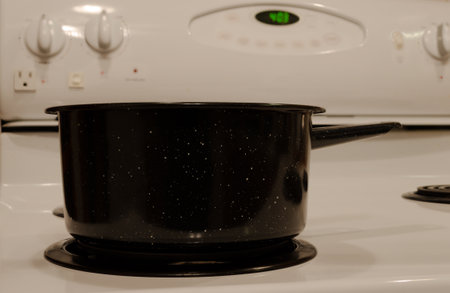 Front view of a single speckled vintage pot on a white electric stove out of focus in the backgroundの写真素材