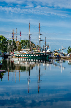 Tall Ships and their reflection on a harbor on a summer day with a lightly clouded blue sky.の写真素材