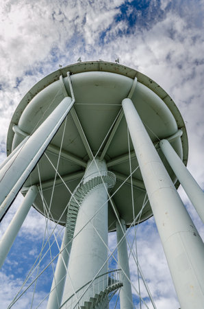 Underside portrait view of a water tower against a cloud filled sky showing winding spiral stairs on the outside of the center column.の写真素材