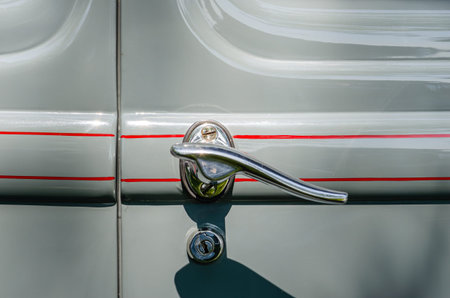 Close-up of a vintage gray car's door handle and door lock with red pinstripes