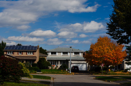 Two storey homes on a residential street, one with solar panels under a blue cloudy sky.