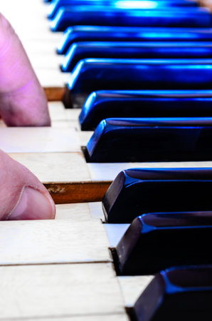 Man 's two fingers shown playing piano's ivory keys receding into the background