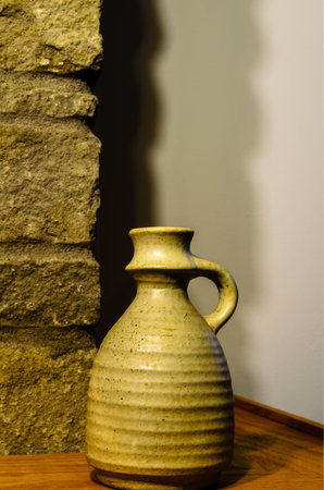 Close-up of a single clay vase on a fireplace mantle corner against shadows on an interior wall.