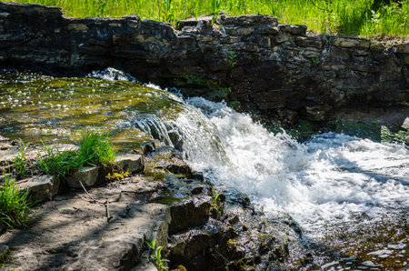 Waterfall cascading on a small stream along a stone wall on a bright summer dayの写真素材