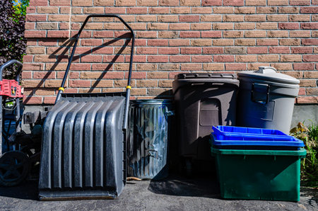 Outside collection of household garbage and recycling bins next to an exterior brick wall