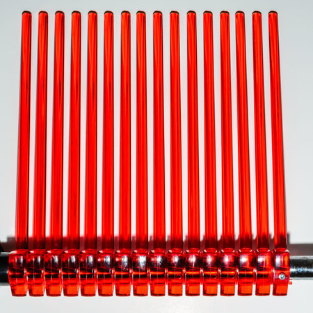 Abstract side view of rows of bright red acrylic rods from a drying rack on a white background.の写真素材