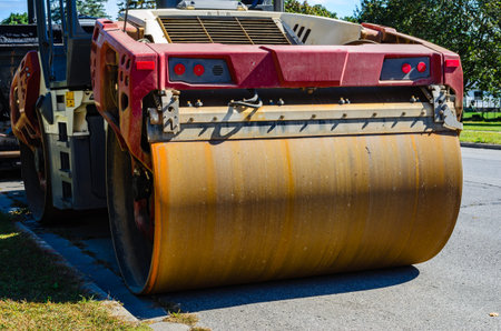 Rusty large front roller on a vibratory compactor parked on a city street in the daytime.