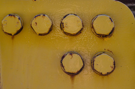 Close-up of six large rusty bolts on a yellow flange showing the old paint.