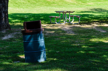 Picnic table and garbage can in a shady public park with green grassの写真素材