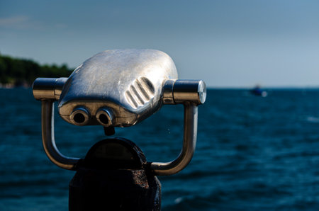 Selective focus close-up rear view of aluminum tourist viewer binoculars with water and boat in the background.の写真素材