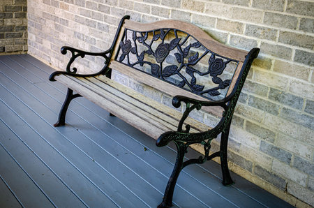 Vintage wood and wrought iron bench on a gray wooden porch, against a gray brick wall