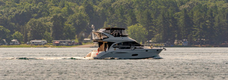 Panorama of a yacht cruising in the St. Lawrence River with an RV camprground in the background on...