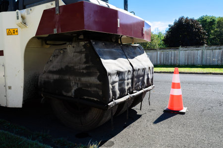 Compaction construction machine on a residential street behind a safety cone with a fence in the...