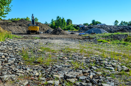 Excavator parked in front of tall piles of fill in a housing development with flat rocks in the...