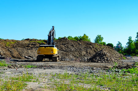 Excavator parked in front of tall piles of fill in a housing developmentunder a clear blue summer...