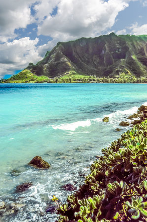 Coastal lagoon in Hawaii with turquoise water and a volcanic mountain in the background under a...